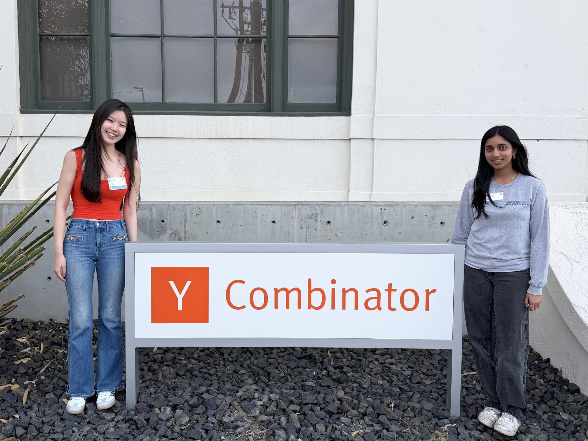 Hannah and Medha standing on either side of the Y Combinator sign